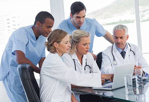 A group of clinicians discusses an issue while looking at a desktop computer.