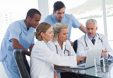 A group of clinicians discusses an issue while looking at a desktop computer. A group of clinicians discusses an issue while looking at a desktop computer.
