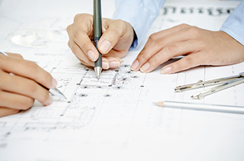 Hands are shown working on a blueprint set on a table.